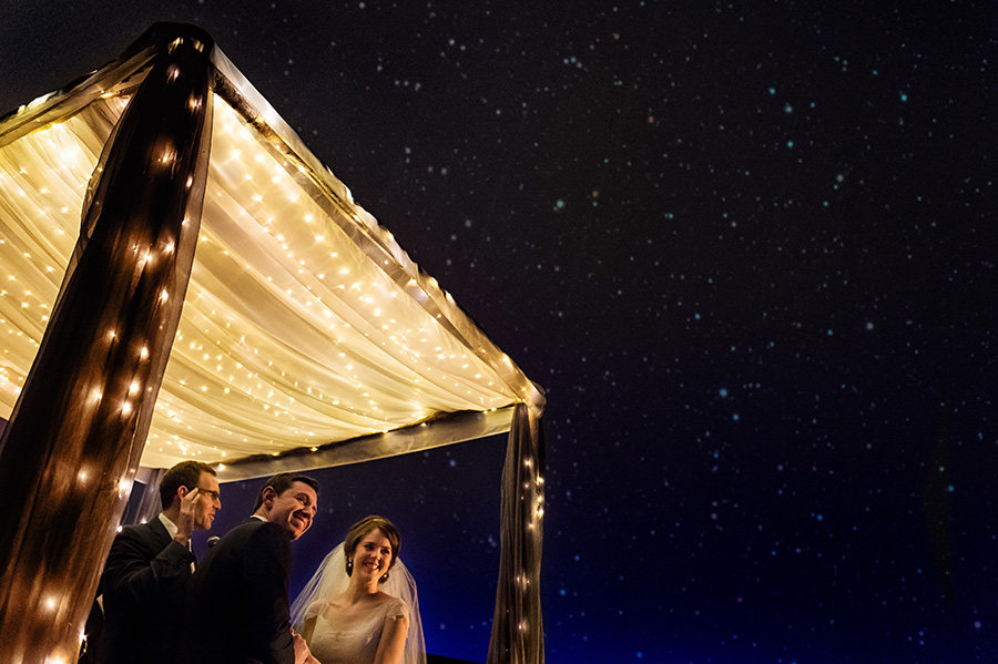 Bride and groom look out at stars during wedding ceremony in Planetarium at Franklin Institute ceremony.