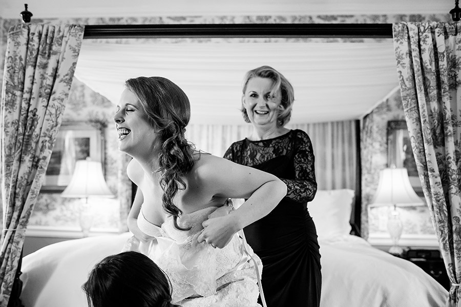 Mother of the bride and bride laughing as she gets into her wedding dress.