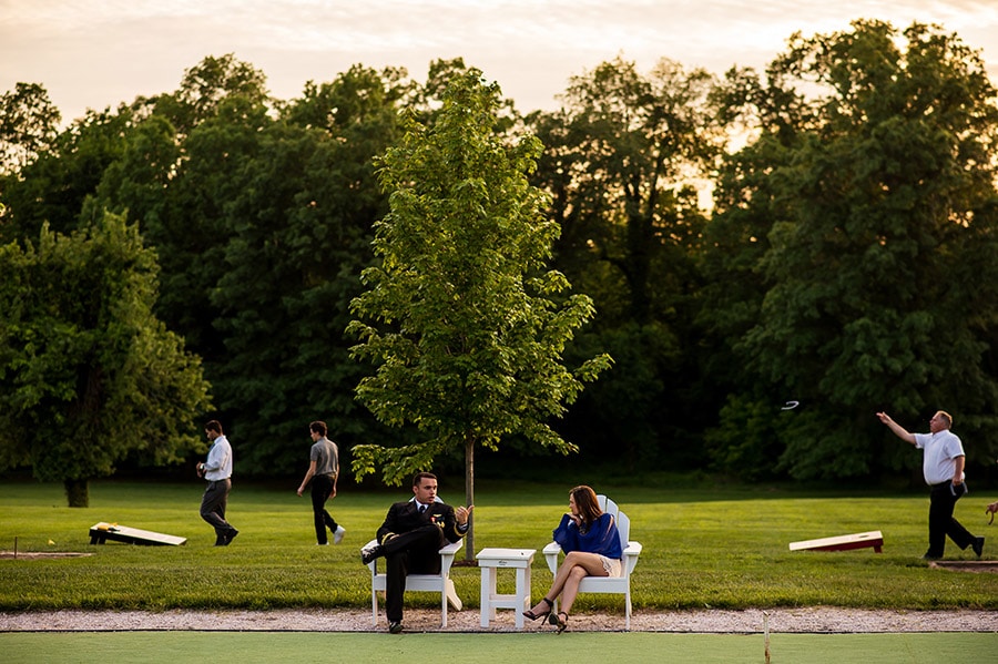 Wedding guests enjoy cocktail hour sitting on chairs and playing lawn games.
