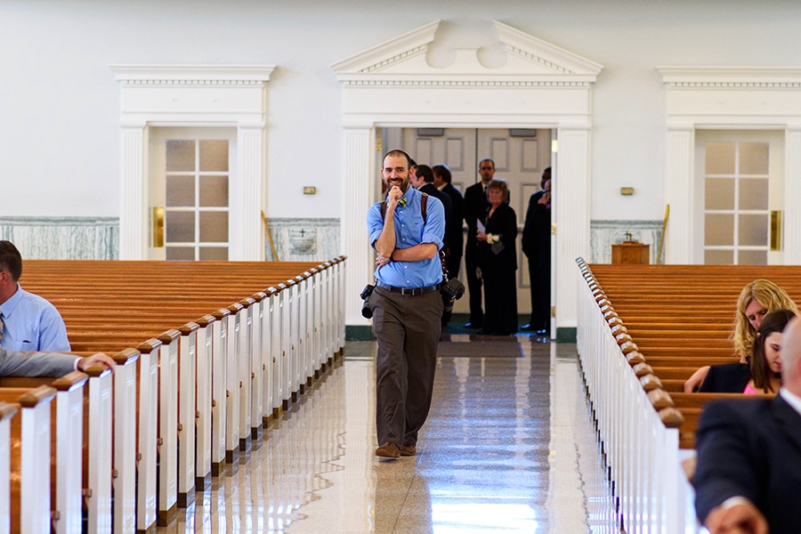 Photographer doing test shot walking down aisle in church on wedding day.