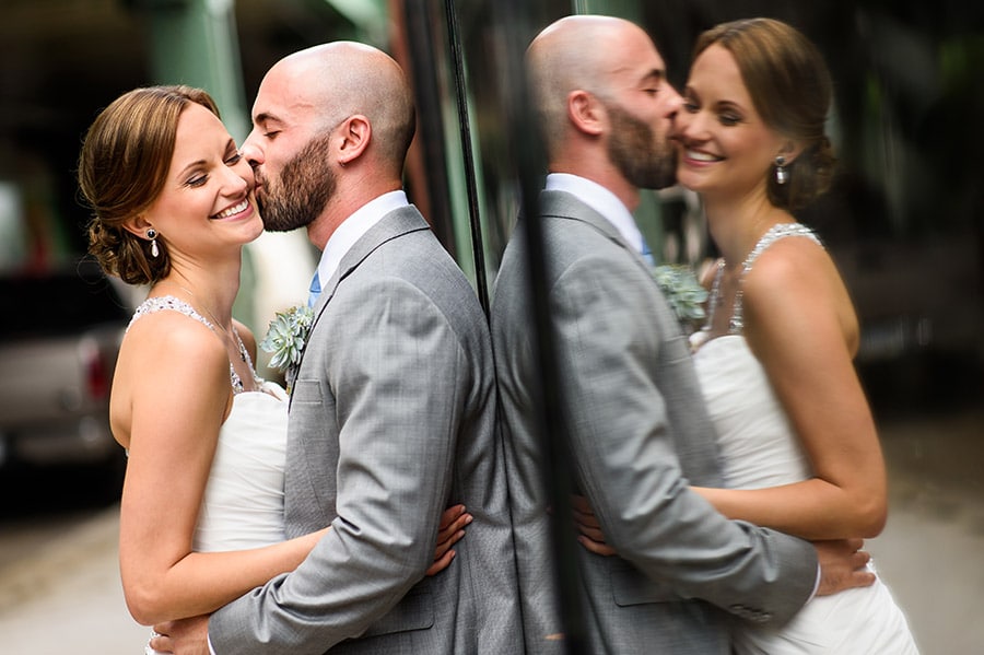 Reflection of groom kissing bride on cheek.