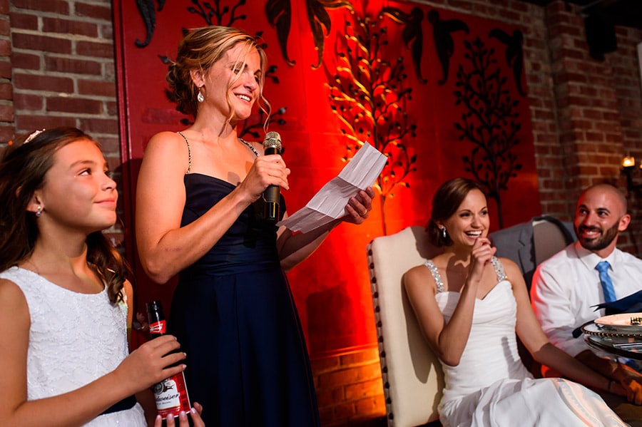 Bride and groom laugh at maid of honor during wedding speech.