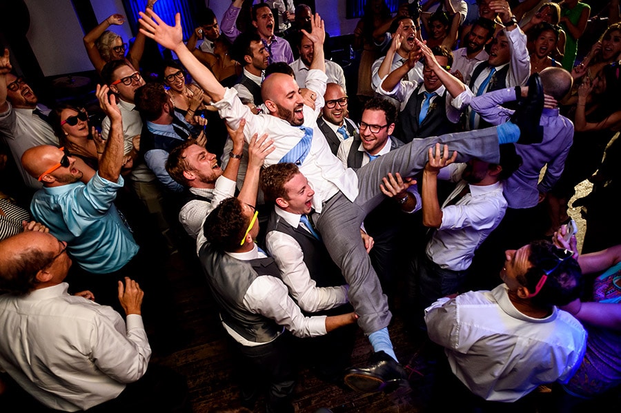 Groomsmen throw groom into air during wedding reception.