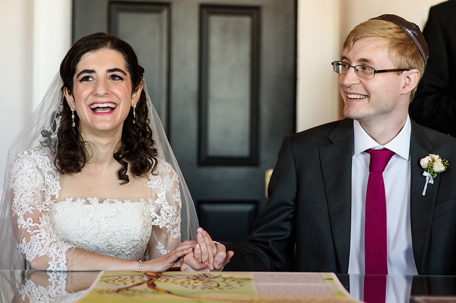 Excited bride and groom laugh as they sign their Ketubah.