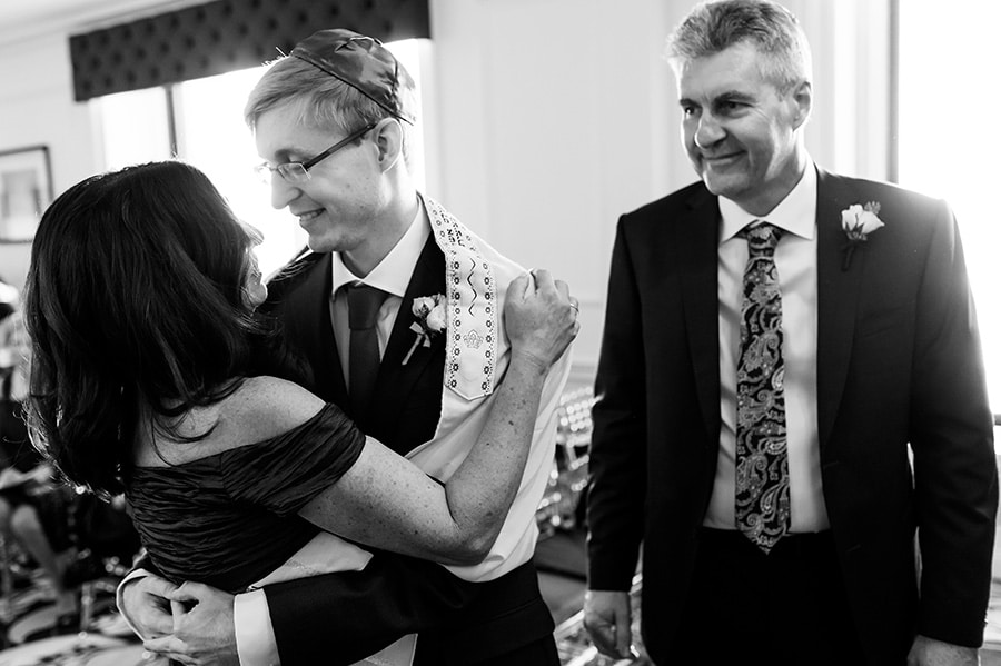 Groom hugs mother as dad looks on after they walked him down the aisle for a Jewish ceremony.