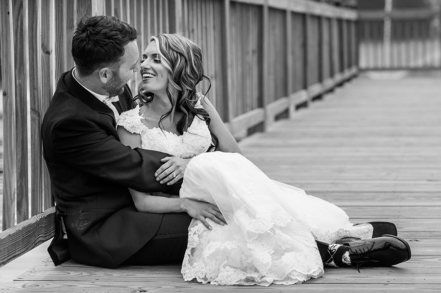 Bride and groom snuggle on dock.