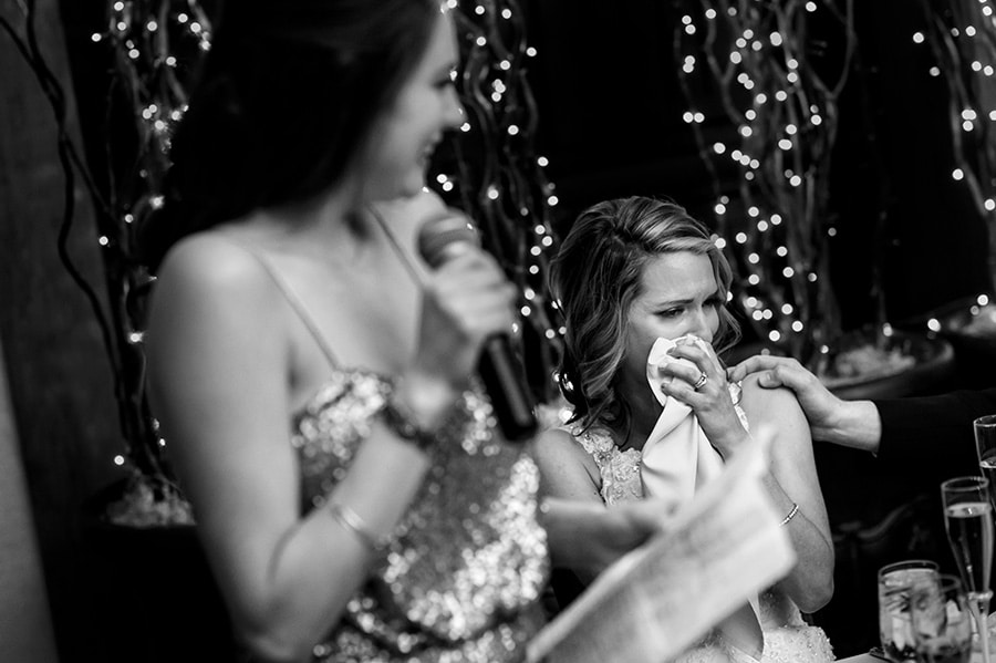 Bride wipes tears away during wedding toast by maid of honor.