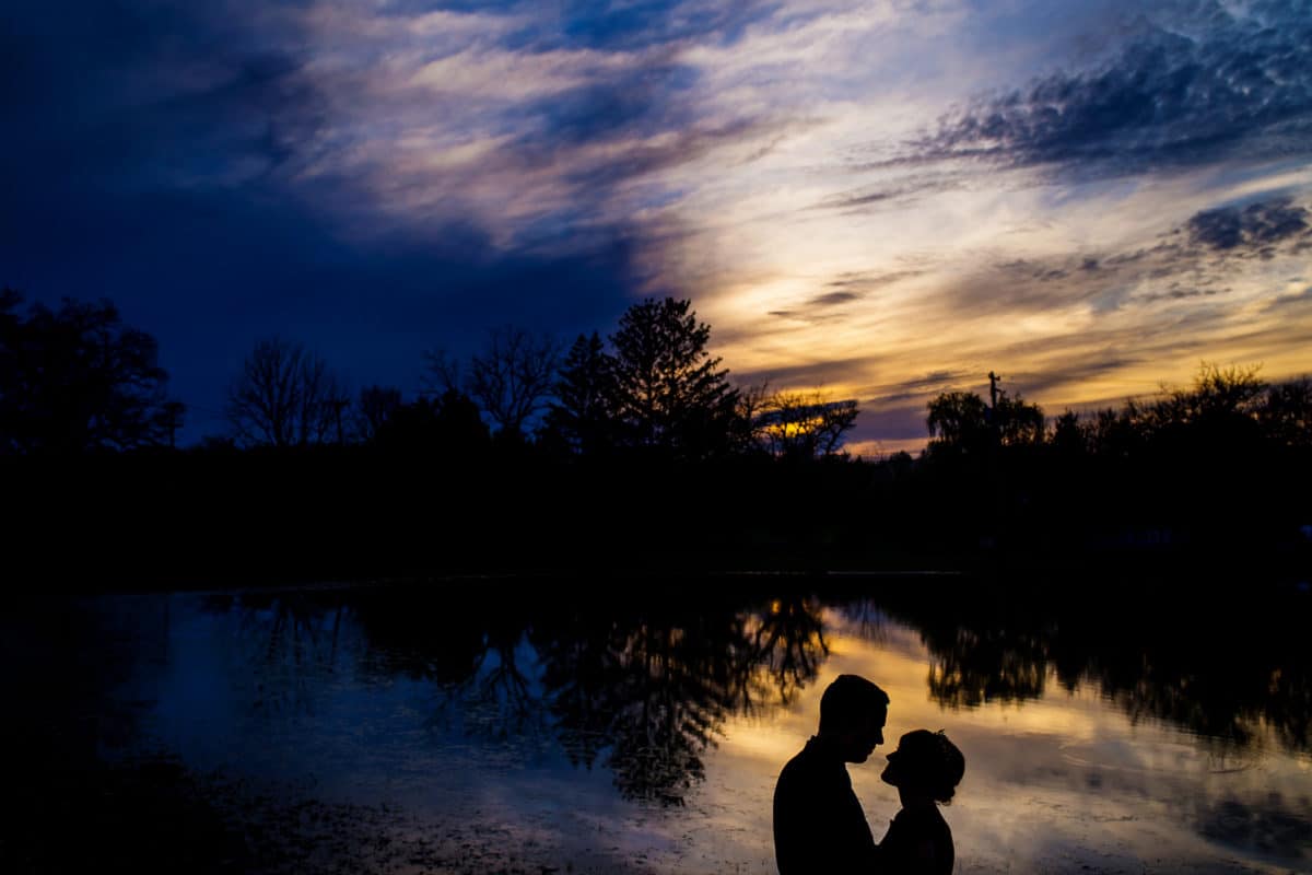 Silhouette of a bride and groom by a lake at sunset.
