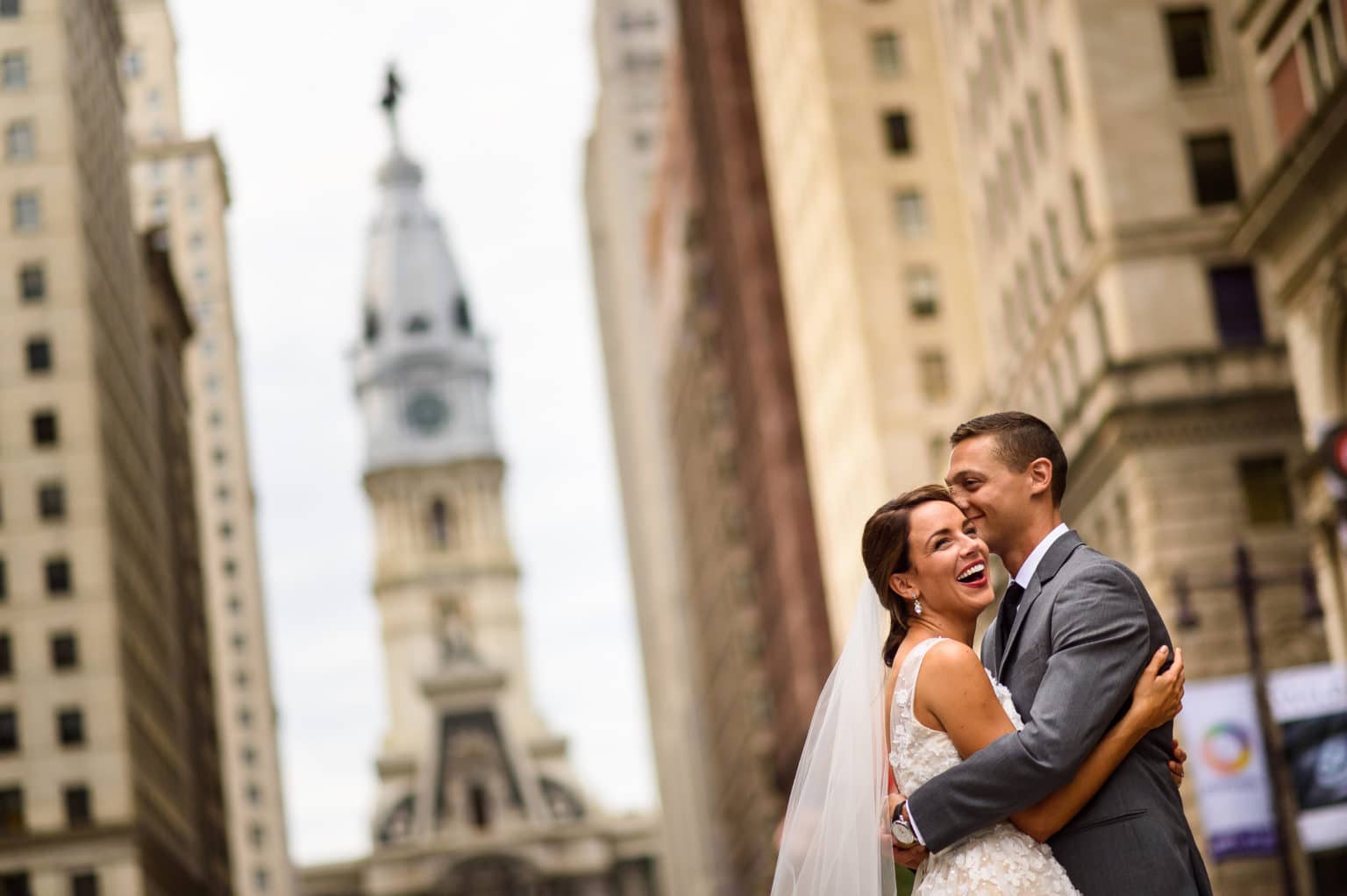 Bride and groom hug each other with Philadelphia's City Hall in the background.