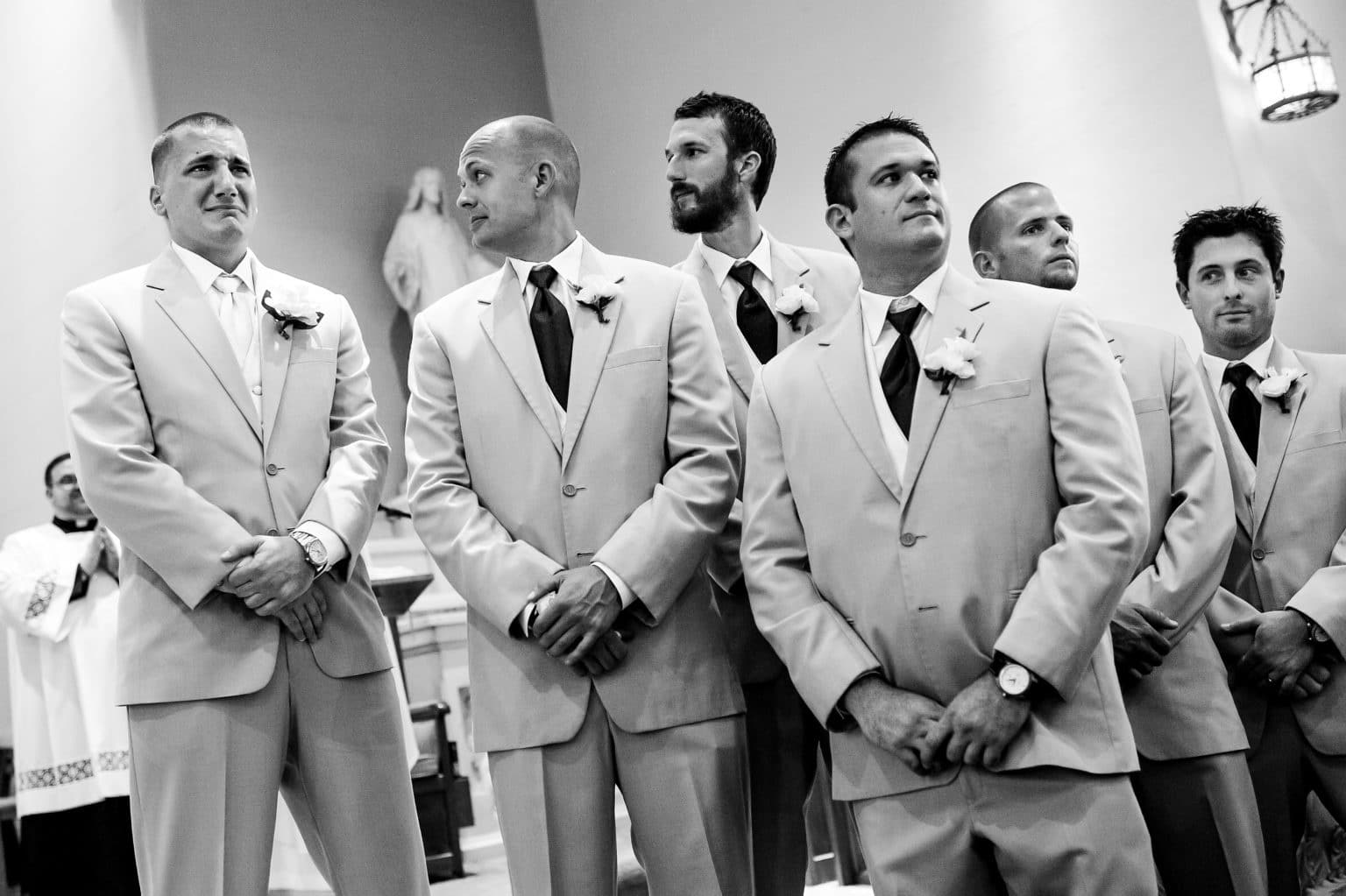 Give groomsmen look at crying groom who sees his bride walking down the aisle towards him.