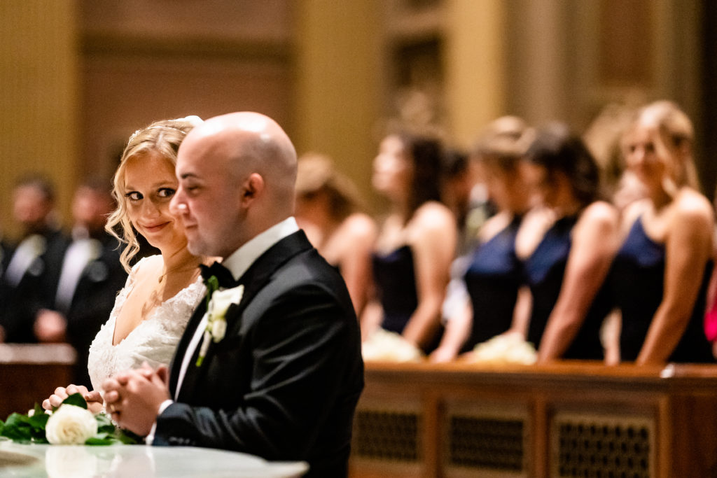 Bride sneaks a glance at groom while praying to blessed mother in the Cathedral Basilica in Philadelphia, Pennsylvania.